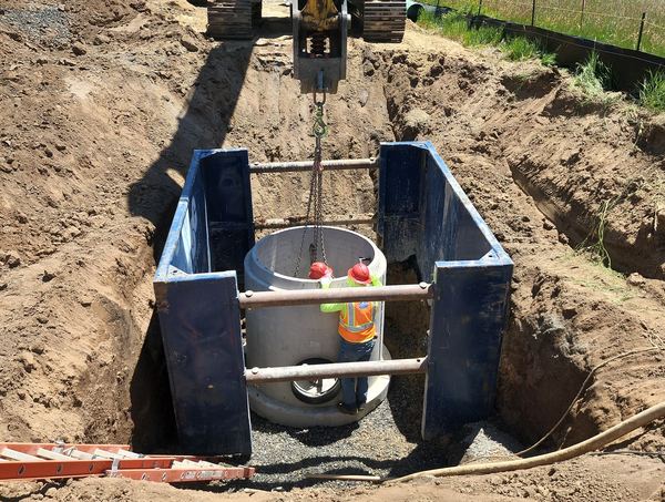 Excavator setting a manhole inside a trench box